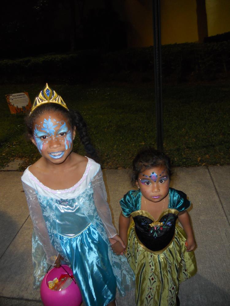 Girl with blue face paint and blue princess costume holding hands with younger girl in princess costume